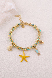 Bracelet doré Awen maille tressée avec cordon et pendentifs étoile de mer, coquillages et poisson - Bijou photographié sur fond en mur blanc