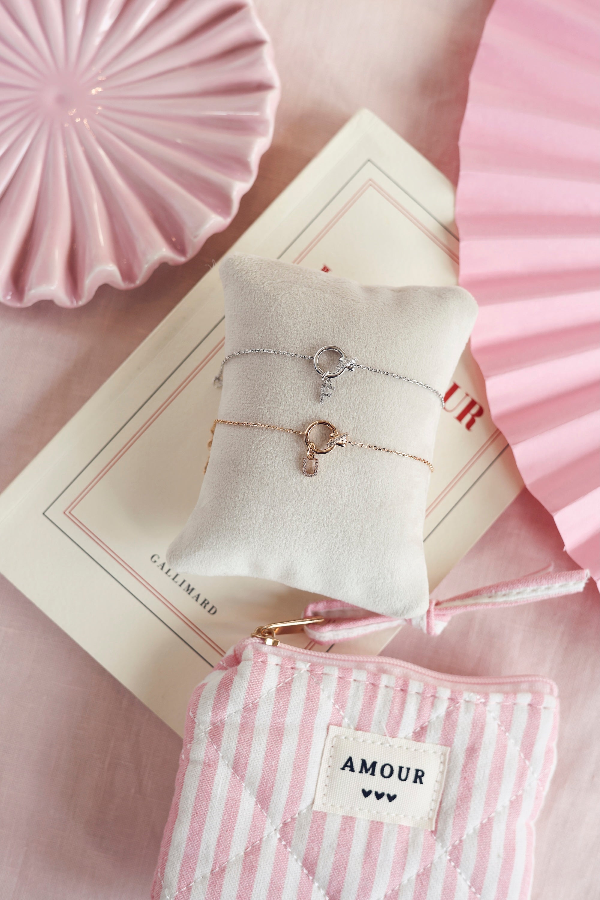 Bracelet personnalisable en argent Kaïs anneau avec nœud orné de zircons pour lettres de l'alphabet et charms - Bijou photographié sur un coussin avec des décorations roses