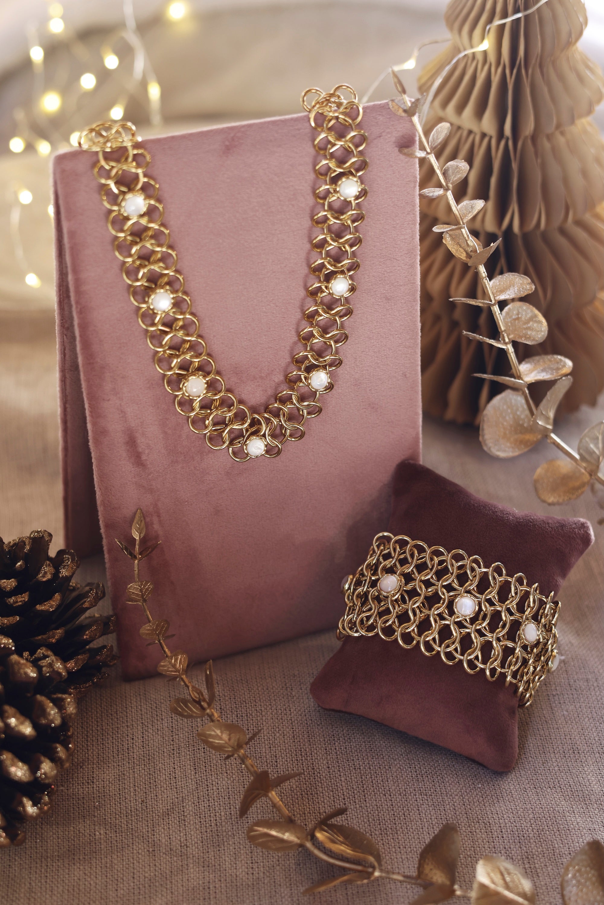Bracelet manchette doré Dolli en maille épaisse orné de nacres - Bijou photographié sur un présentoir en velours rose foncé avec des décorations de Noël