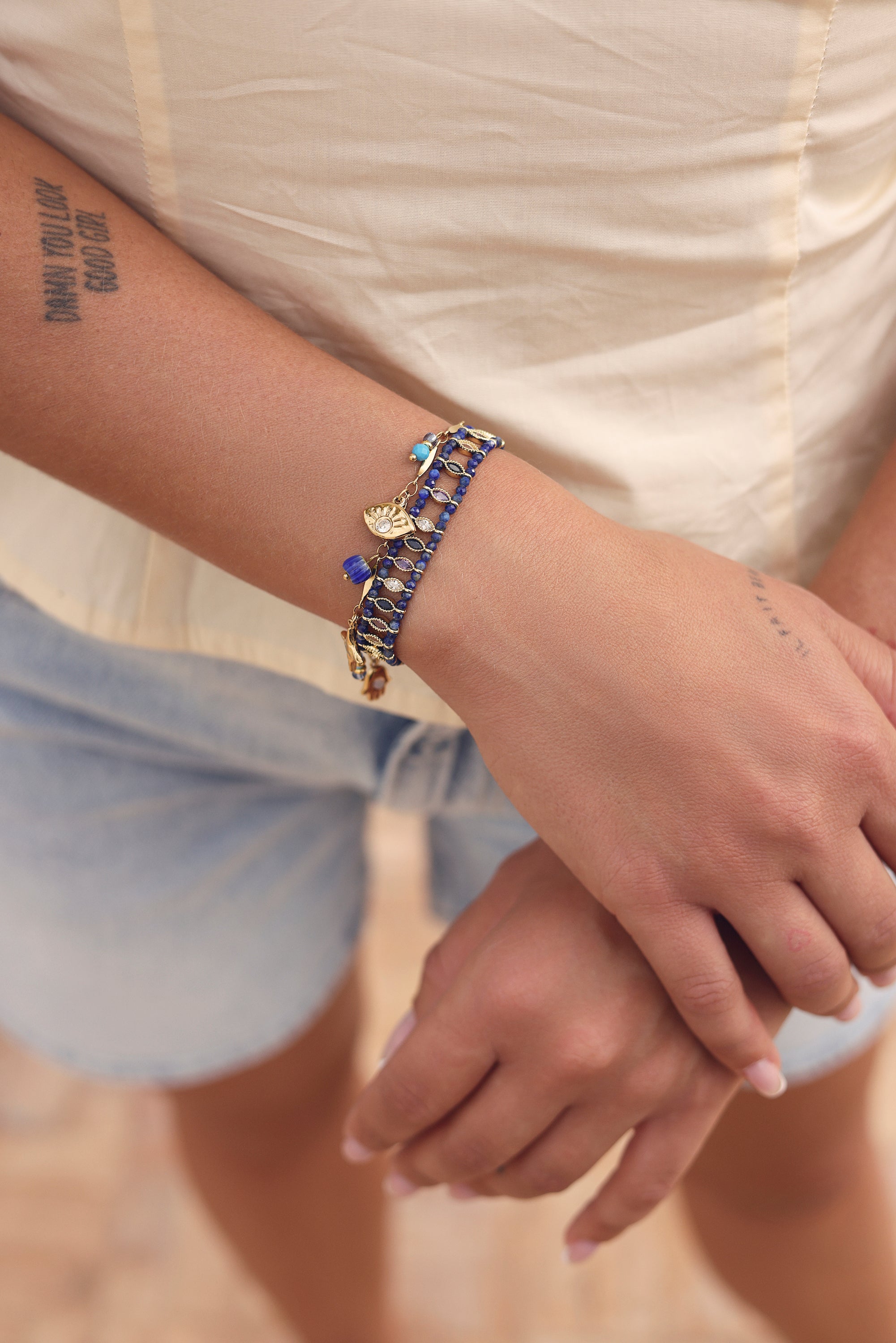 Bracelet doré Emery orné d’une étoile en sodalite, d’une main, d’un œil serti de zircon, d’une étoile polaire et de pendentifs en pierres bleues et en émail - Bijou porté
