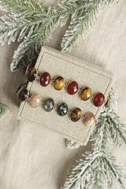 Bracelet doré Favelia rubis zoisite orné de pierres naturelles - Bijou photographié sur un présentoir en lin gris avec des branches de sapins enneigées