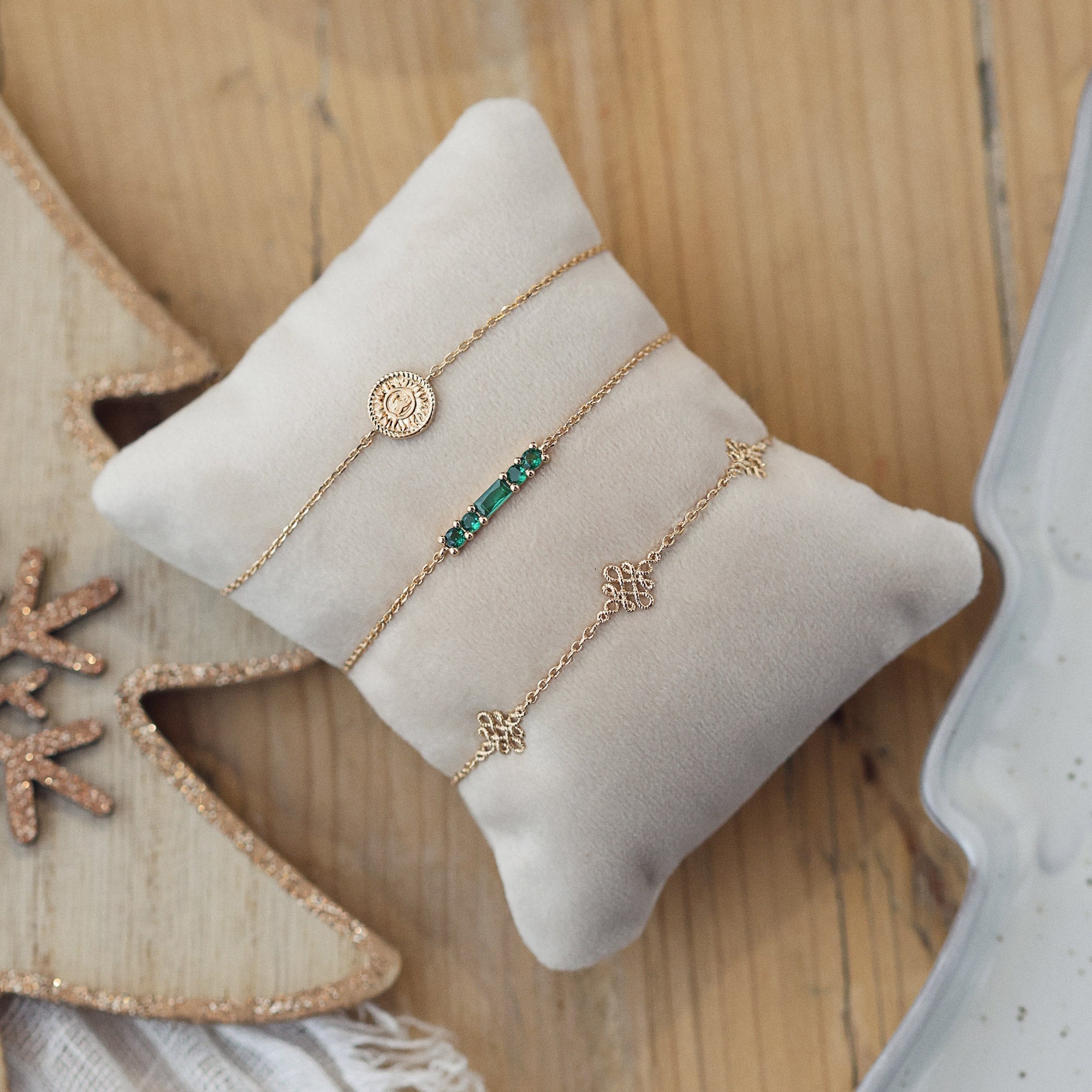 Bracelet doré Janice en plaqué or avec motifs infini entrelacés - Bijou photographié sur petit coussin beige posé sur une table en bois avec des sapins de Noël en bois décorés de paillettes