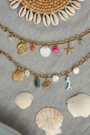 Bracelet doré Larysa pendentifs coquillage en nacre, coquillage doré, étoile de mer et pierres colorées - Bijou photographié dans un décor estival