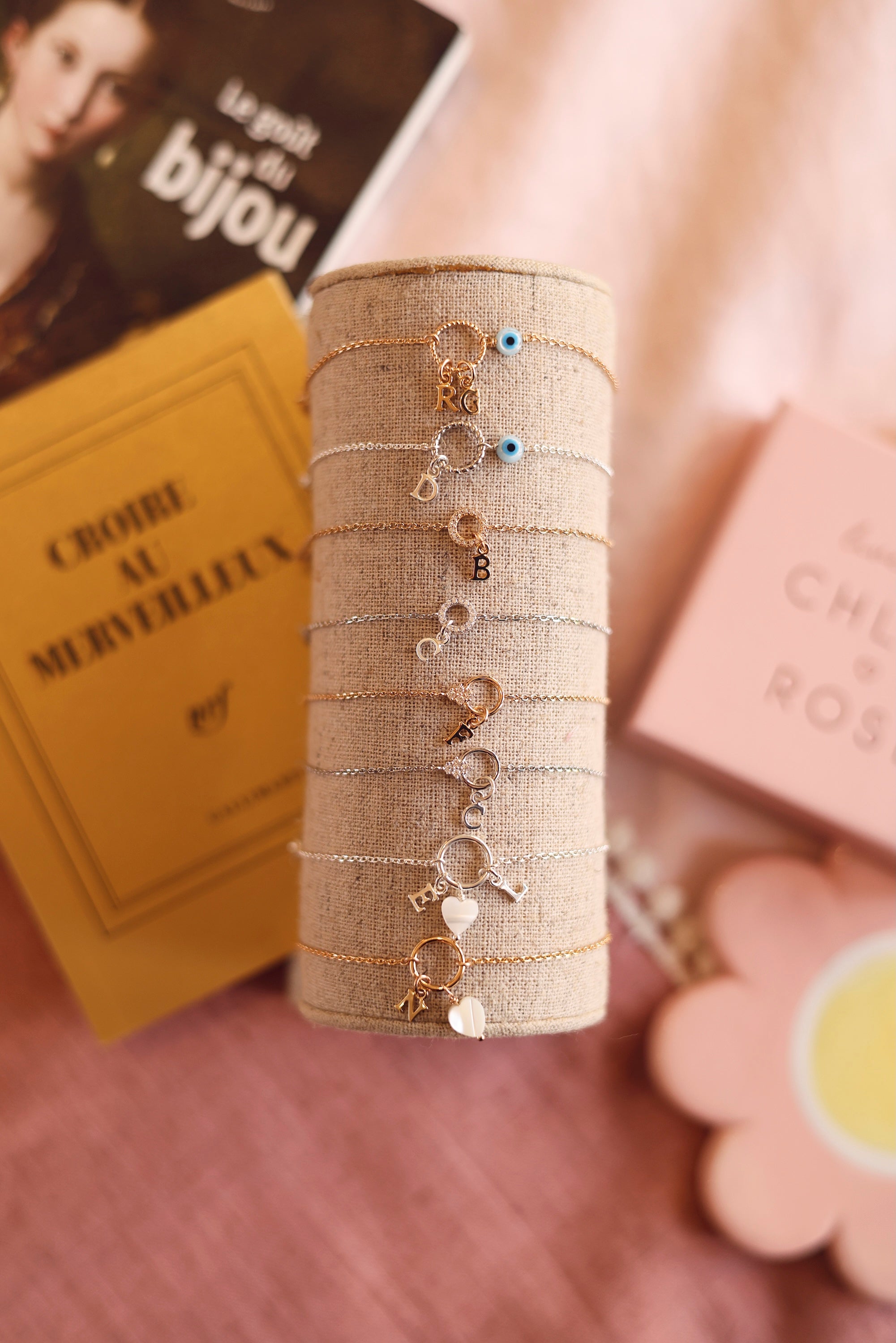 Bracelet personnalisable doré Lilou protect avec anneau torsadé et œil protecteur en nacre pour lettres de l'alphabet et charms - Bijou photographié sur un présentoir en lin avec d'autres bracelets personnalisables