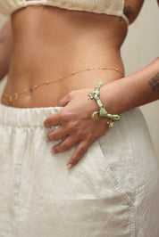 Bracelet doré Yarina bandana vert avec pendentifs soleil, trèfle, cœur, oiseau et fleur sertie d'un zircon - Bijou porté