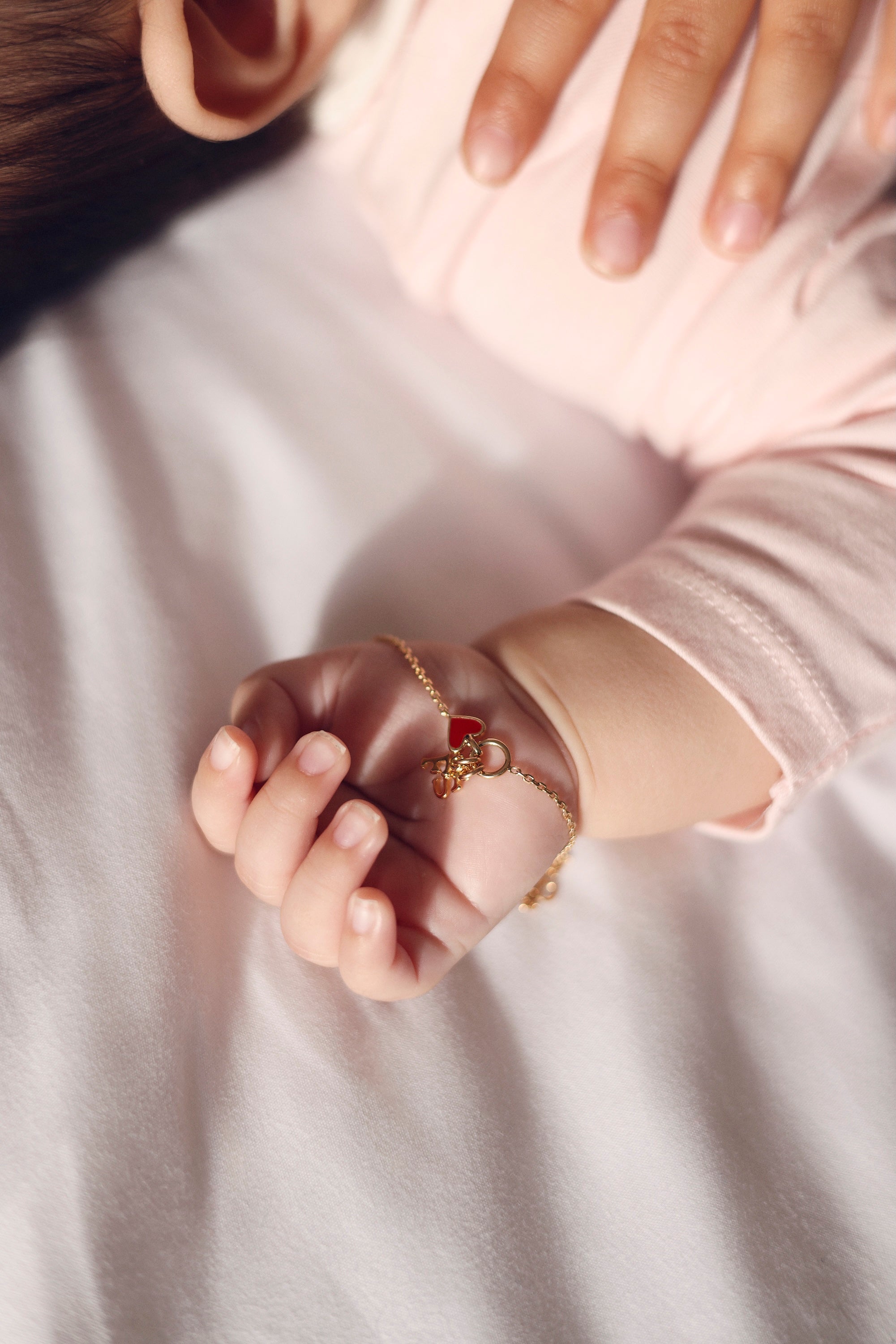 Bracelet personnalisable doré Lilou passion avec anneau et pendentif cœur rouge pour lettres de l’alphabet et charms - Bijou photographié dans la main d'un bébé