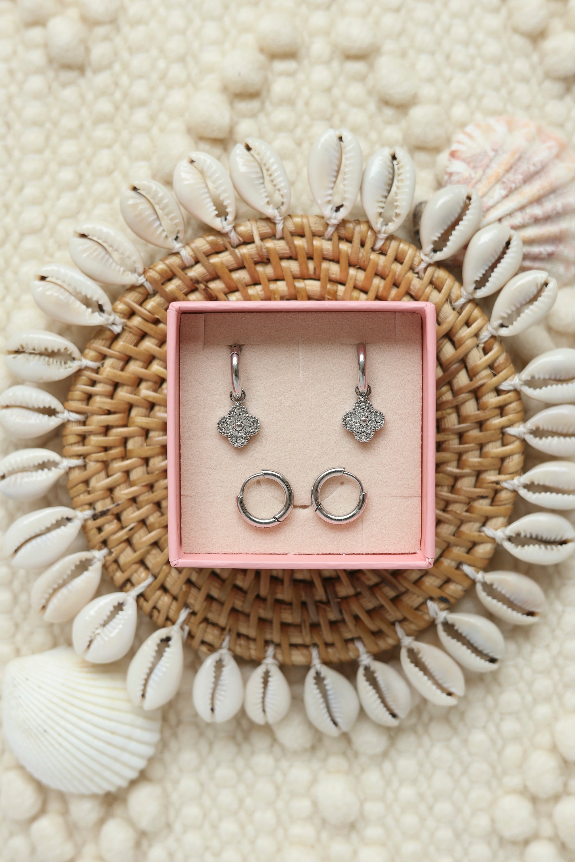 Coffret de parure de bijoux Shore comprenant une paire de mini créoles argentées ornées d’une fleur sertie de zircons ainsi qu’une paire de créoles simples - Bijoux photographiés dans un décor estival