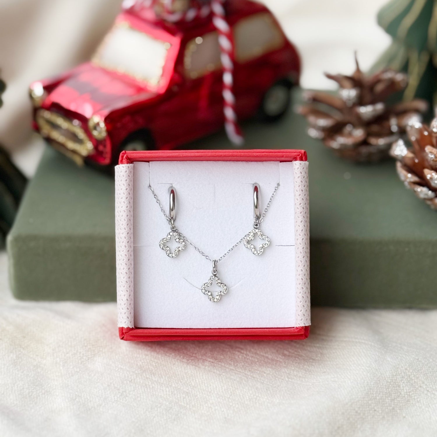 Coffret de parure Lovely comprenant une paire de mini créoles et un collier argentés, ornés d’un pendentif trèfle serti de zircons - Bijoux photographiés dans un écrin à bijoux rouge dans une ambiance de Noël