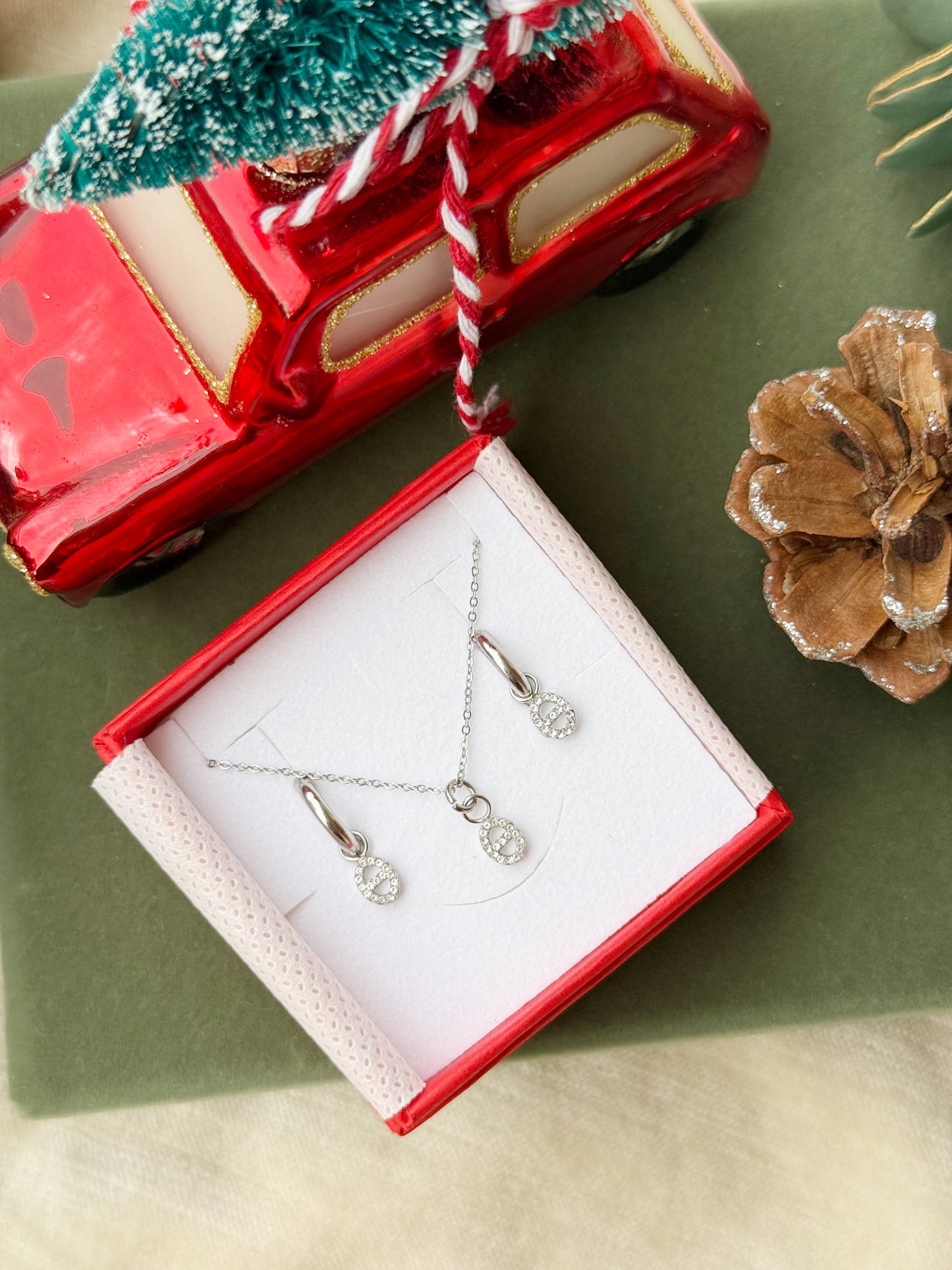 Coffret de parure Maille marine comprenant une paire de mini créoles et un collier argentés, ornés d’un pendentif maille marine serti de zircons - Bijoux photographiés dans un écrin à bijoux rouge dans une ambiance de Noël
