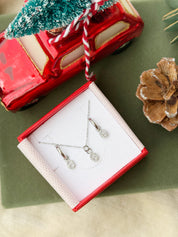 Coffret de parure Maille marine comprenant une paire de mini créoles et un collier argentés, ornés d’un pendentif maille marine serti de zircons - Bijoux photographiés dans un écrin à bijoux rouge dans une ambiance de Noël
