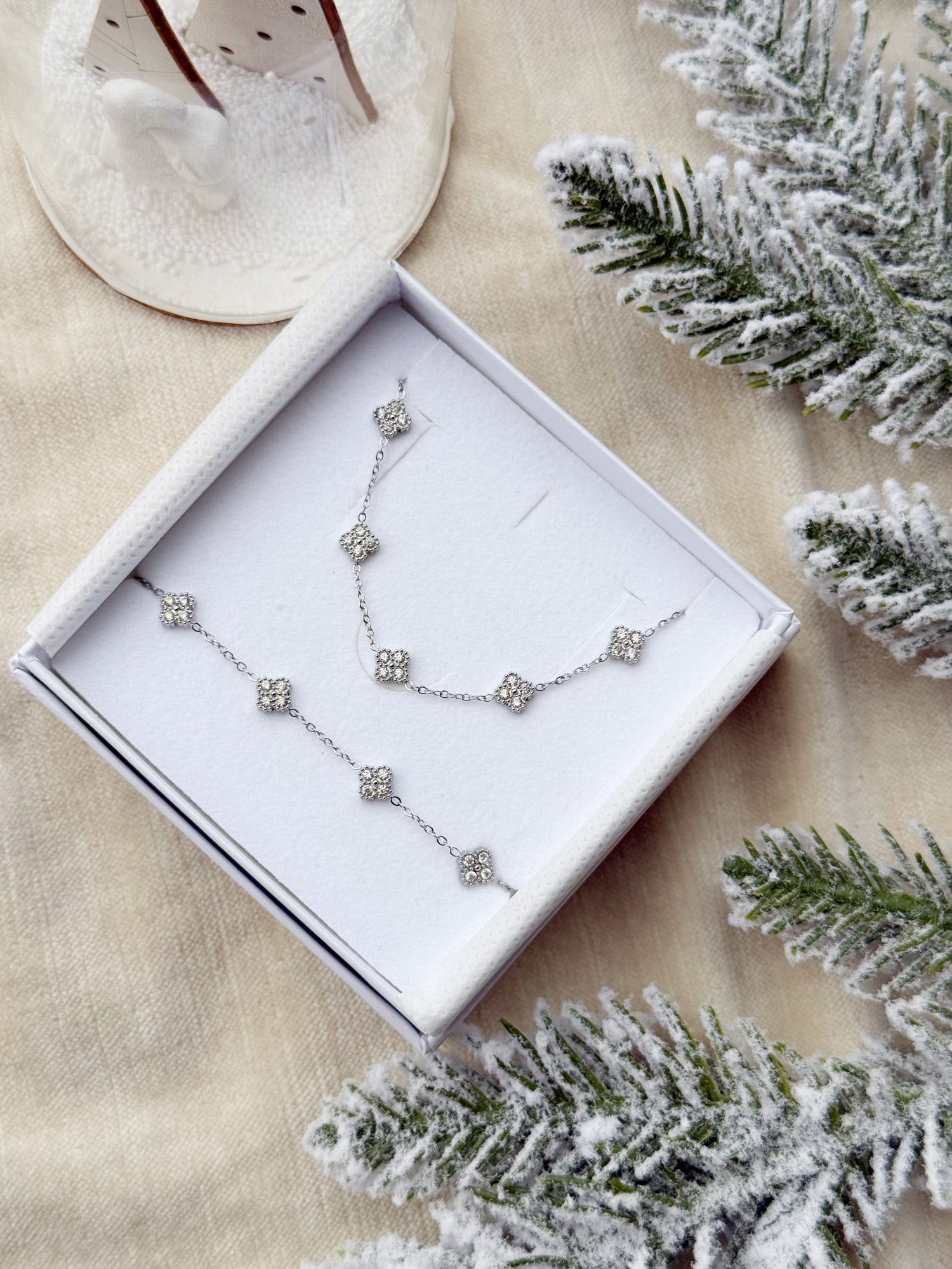 Coffret de parure Dolce comprenant un collier et un bracelet argentés, ornés de petites fleurs serties de zircons - Bijoux photographiés dans un écrin à bijoux blanc dans une ambiance de Noël