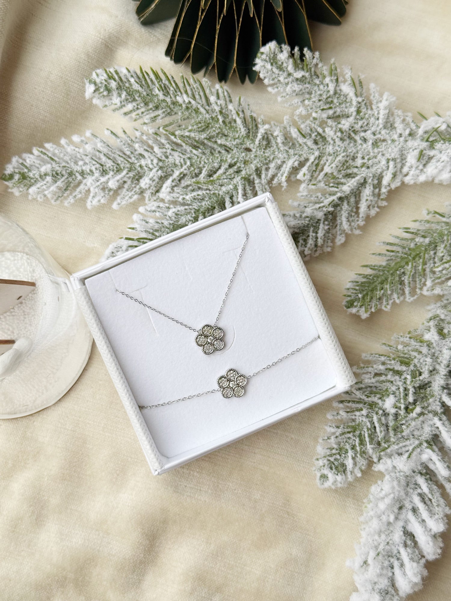 Coffret de parure Shine comprenant un collier et un bracelet argentés, ornés d’une fleur sertie de zircons - Bijoux photographiés dans un écrin à bijoux blanc dans une ambiance de Noël