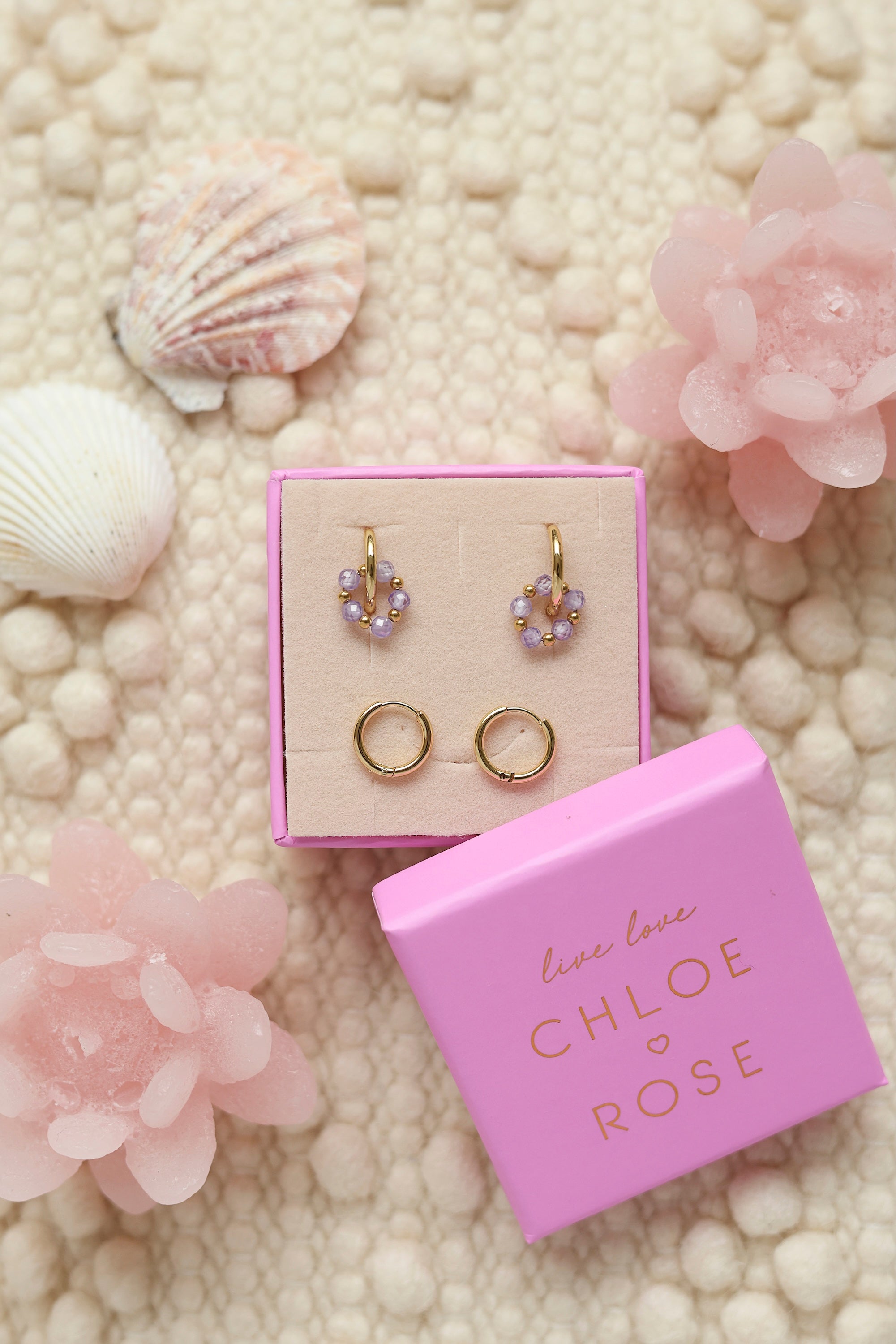 Coffret de parure de bijoux Sunday lila comprenant une paire de mini créoles dorées ornées d'un anneau en perles dorées et lila ainsi qu’une paire de créoles simples - Bijoux photographiés dans un décor estival