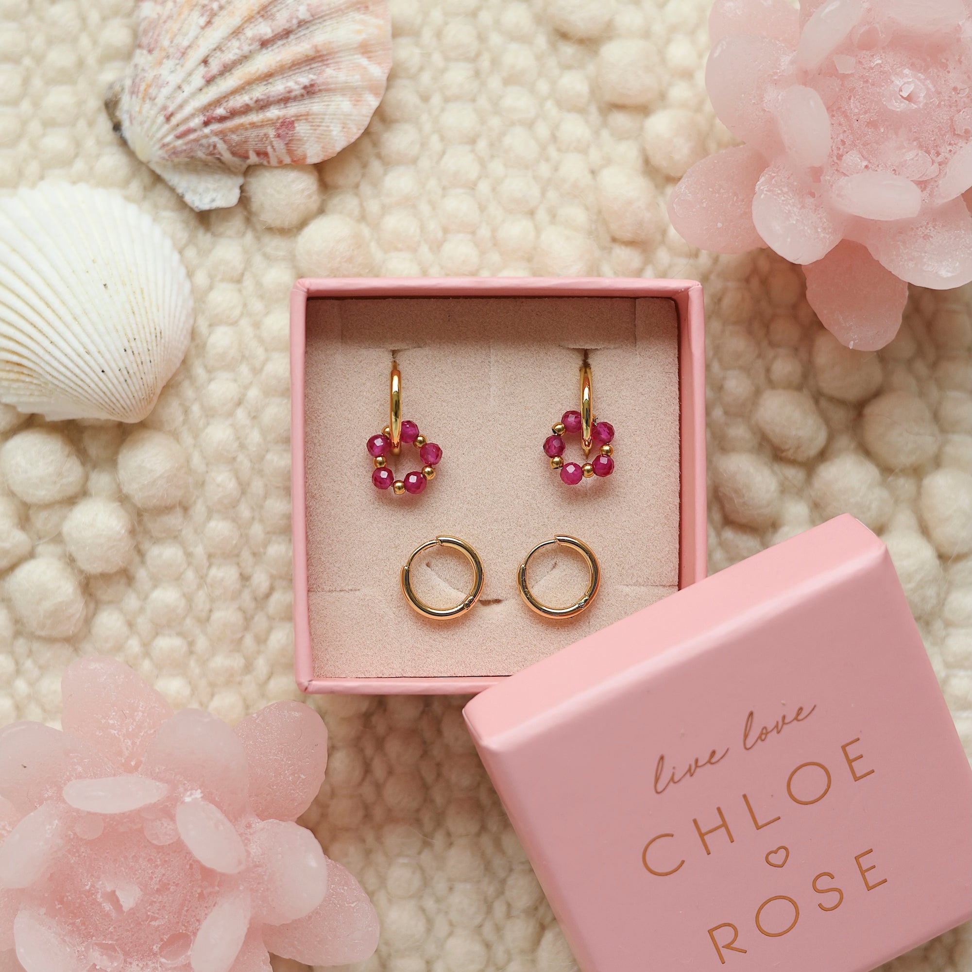 Coffret de parure de bijoux Sunday fuchsia comprenant une paire de mini créoles dorées ornées d'un anneau en perles dorées et fuchsia ainsi qu’une paire de créoles simples - Bijoux photographiés dans un décor estival