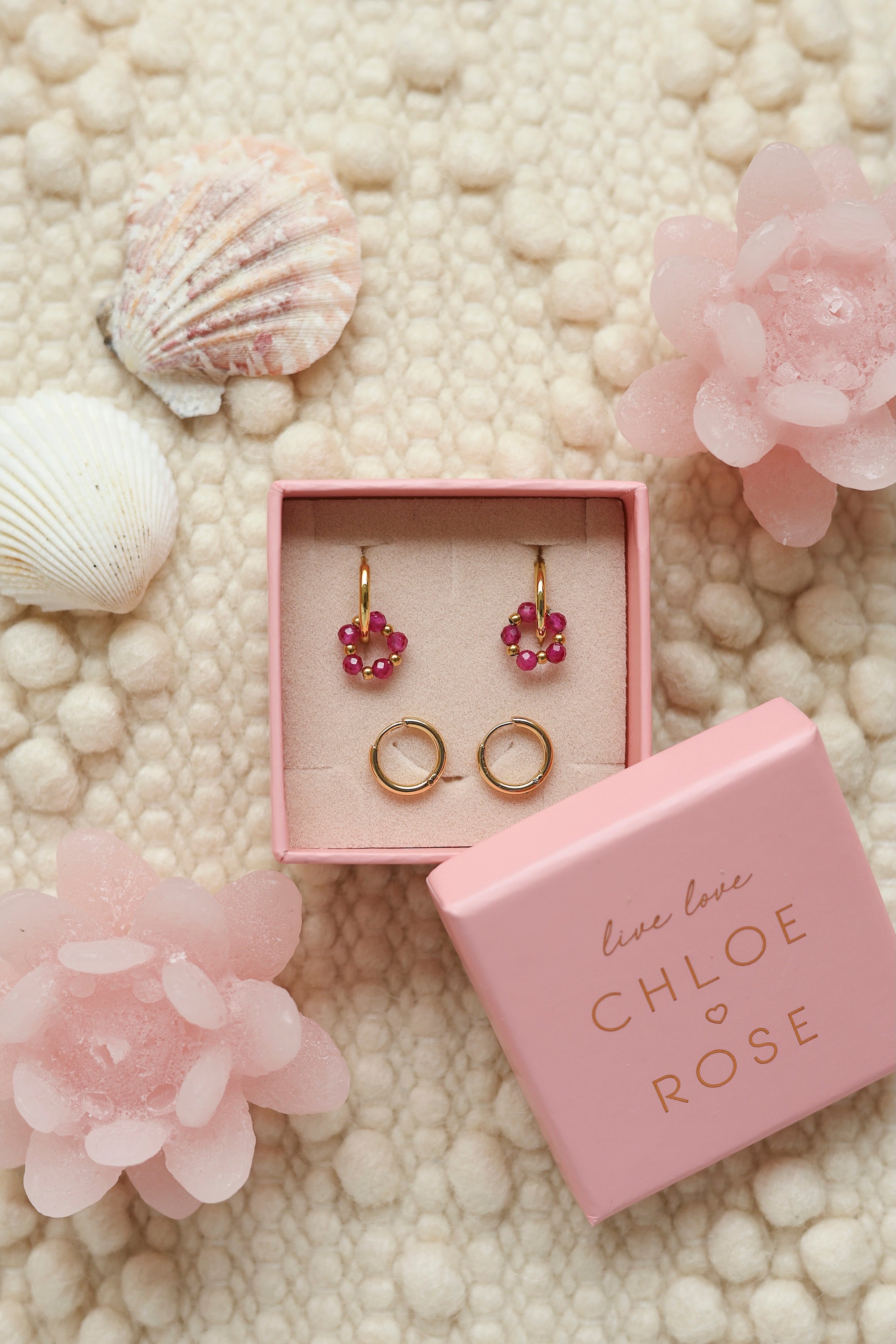 Coffret de parure de bijoux Sunday fuchsia comprenant une paire de mini créoles dorées ornées d'un anneau en perles dorées et fuchsia ainsi qu’une paire de créoles simples - Bijoux photographiés dans un décor estival
