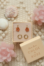 Coffret de parure de bijoux Sunday orange comprenant une paire de mini créoles dorées ornées d'un anneau en perles dorées et orange ainsi qu’une paire de créoles simples - Bijoux photographiés dans un décor estival