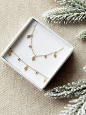 Coffret de parure de bijoux Davia éclair contenant un collier et un bracelet dorés, ornés de petits charms en forme d’éclair sertis de zircons - Bijoux photographiés dans un écrin à bijoux blanc dans une ambiance hivernale