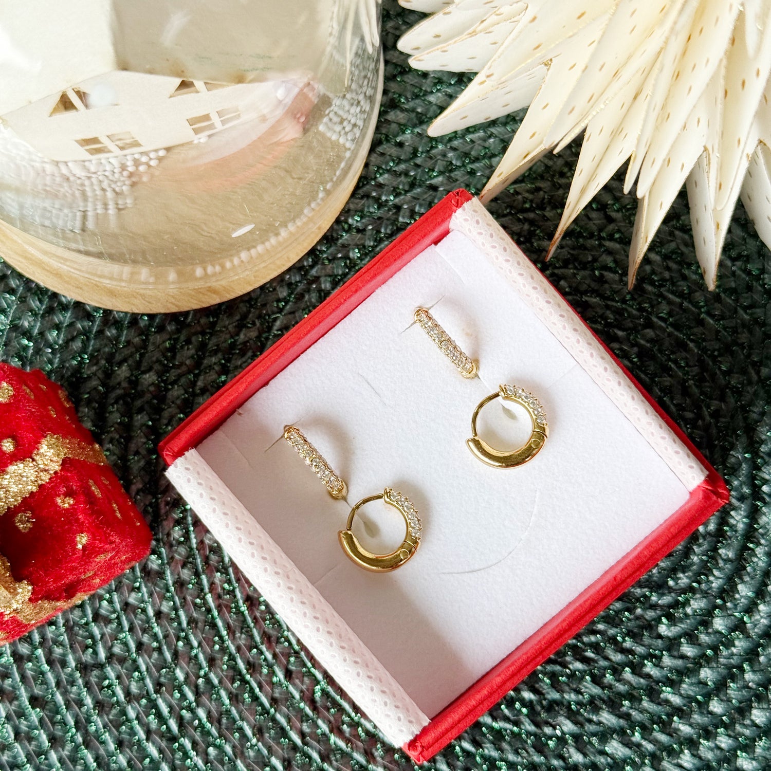 Coffret de parure de bijoux Divine contenant deux paires de mini créoles dorées ornées de zircons - Bijoux photographiés dans un écrin à bijoux rouge dans une ambiance de Noël