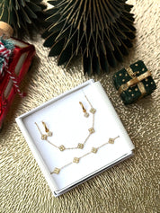 Coffret de parure Dolce comprenant une paire de mini créoles, un collier et un bracelet dorés, ornés de petites fleurs serties de zircons - Bijoux photographiés dans un écrin à bijoux blanc dans une ambiance de Noël
