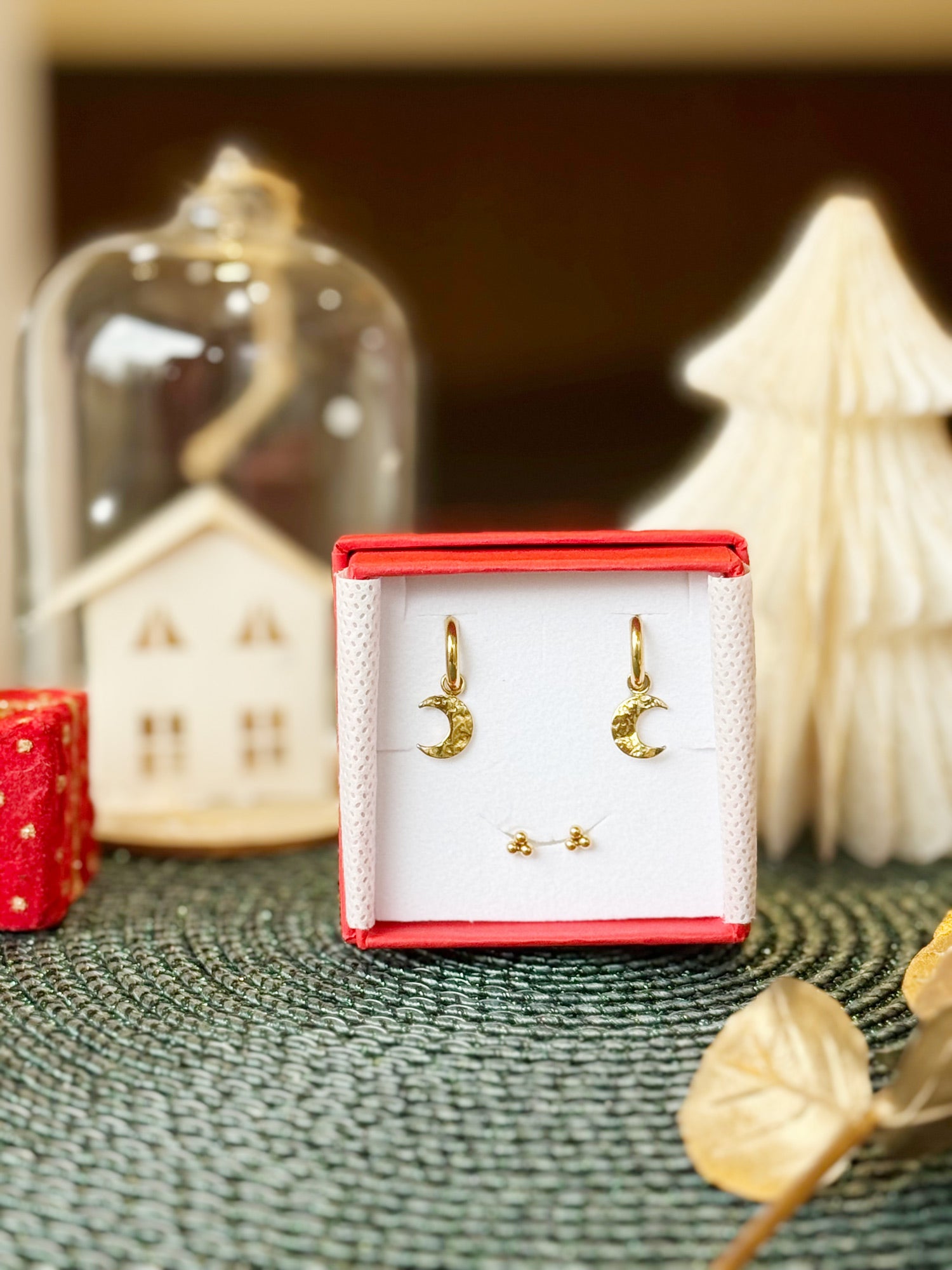 Coffret de parure de bijoux Luna contenant une paire de mini créoles avec des pendentifs lunes et une paire de puces dorées - Bijoux photographiés dans un écrin à bijoux rouge dans une ambiance de Noël