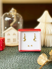 Coffret de parure de bijoux Luna contenant une paire de mini créoles avec des pendentifs lunes et une paire de puces dorées - Bijoux photographiés dans un écrin à bijoux rouge dans une ambiance de Noël