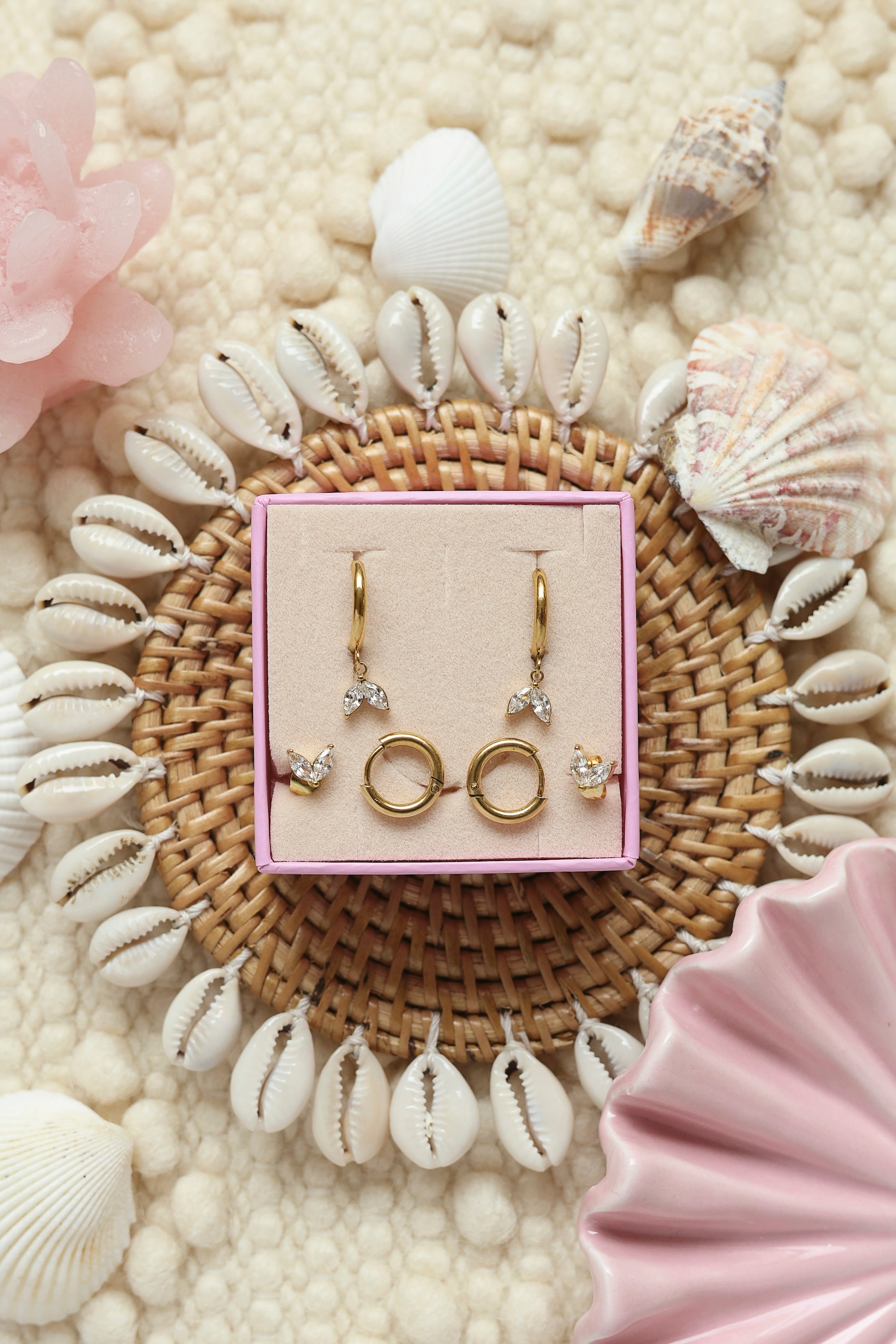 Coffret de parure de bijoux Oasis blanc comprenant une paire de mini créoles dorées ornées d’un pendentif pétales serti de zircons ainsi qu’une paire de créoles simples et une paire de puces assorties - Bijoux photographiés dans un décor estival