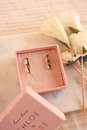 Coffret de parure de bijoux Sara vert contenant deux paires de mini créoles dorées ornées de zircons - Bijoux photographiés dans un écrin à bijoux rose posé sur du marbre blanc avec des fleurs