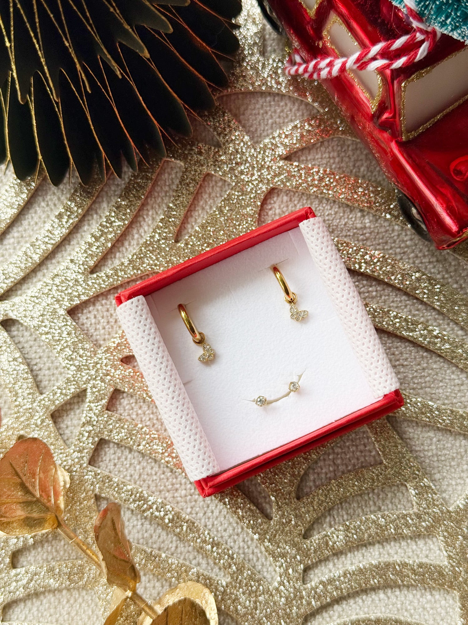 Coffret de parure de bijoux Classy contenant une paire de mini créoles avec des pendentifs papillons et une paire de puces dorées zircons - Bijoux photographié dans un écrin à bijoux rouge dans une ambiance de Noël
