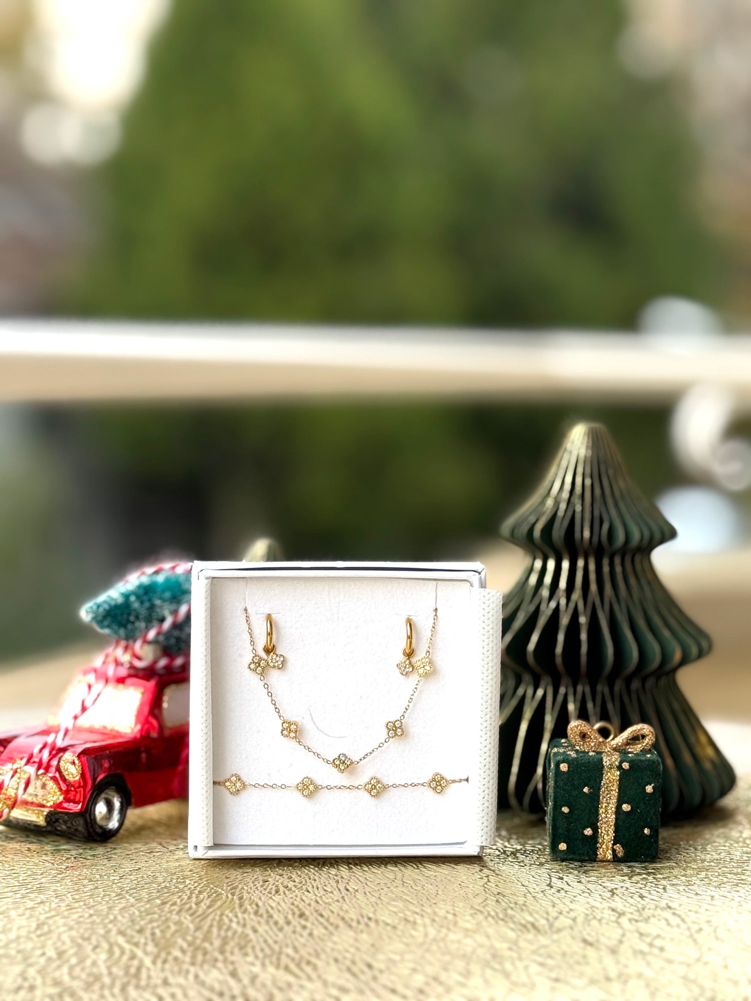 Coffret de parure Dolce comprenant une paire de mini créoles, un collier et un bracelet dorés, ornés de petites fleurs serties de zircons - Bijoux photographiés dans un écrin à bijoux blanc dans une ambiance de Noël