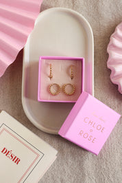 Coffret de parure de bijoux Laperla contenant deux paires de mini créoles dorées perlées - Bijoux photographiés dans un écrin à bijoux rose dans une coupole blanche avec des décorations roses