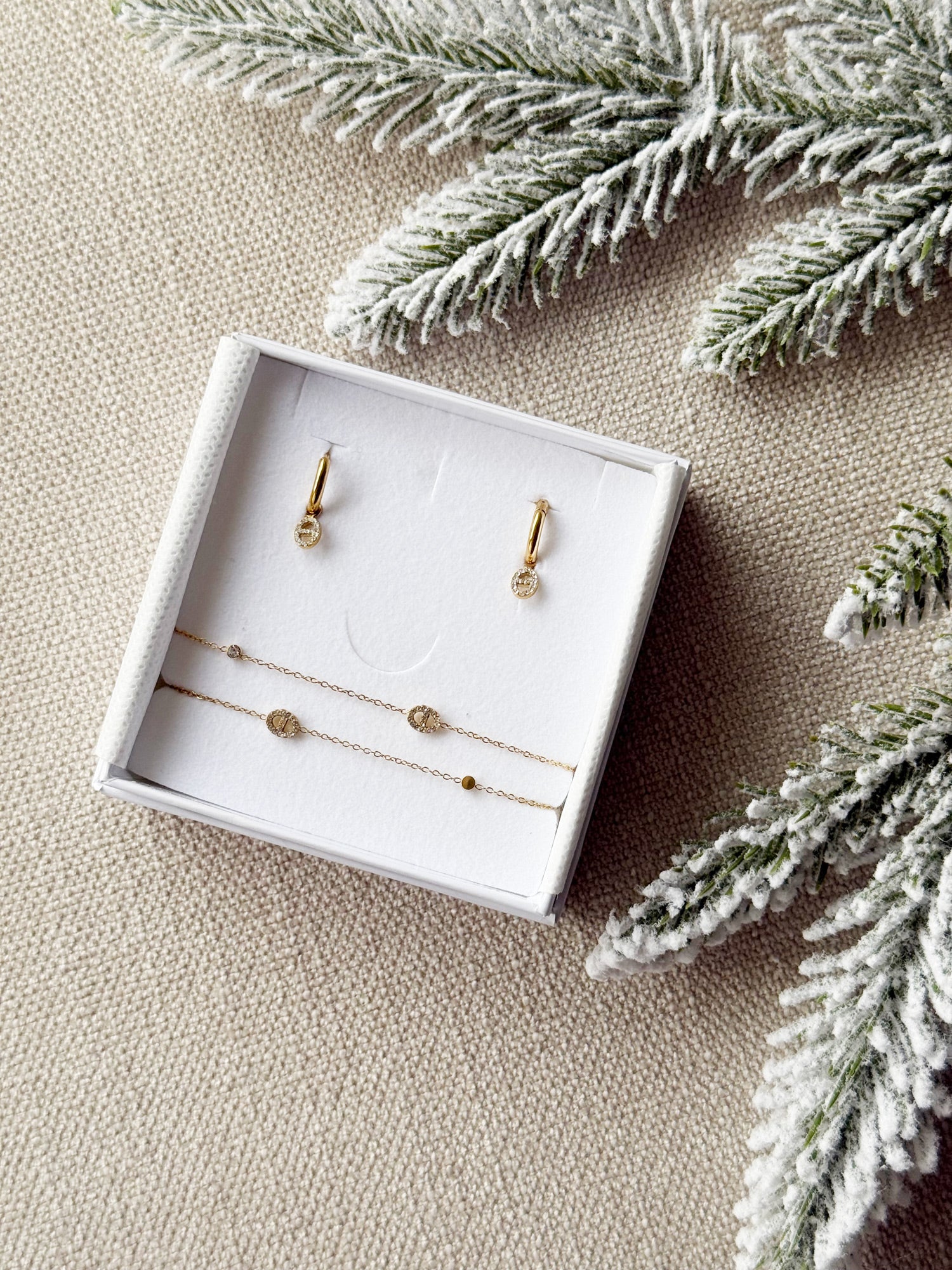 Coffret de parure de bijoux Maille marine contenant une paire de mini créoles avec des pendentifs maille marine et un bracelet double dorés - Bijoux photographiés dans un écrin à bijoux blanc dans une ambiance de Noël