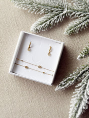 Coffret de parure de bijoux Maille marine contenant une paire de mini créoles avec des pendentifs maille marine et un bracelet double dorés - Bijoux photographiés dans un écrin à bijoux blanc dans une ambiance de Noël