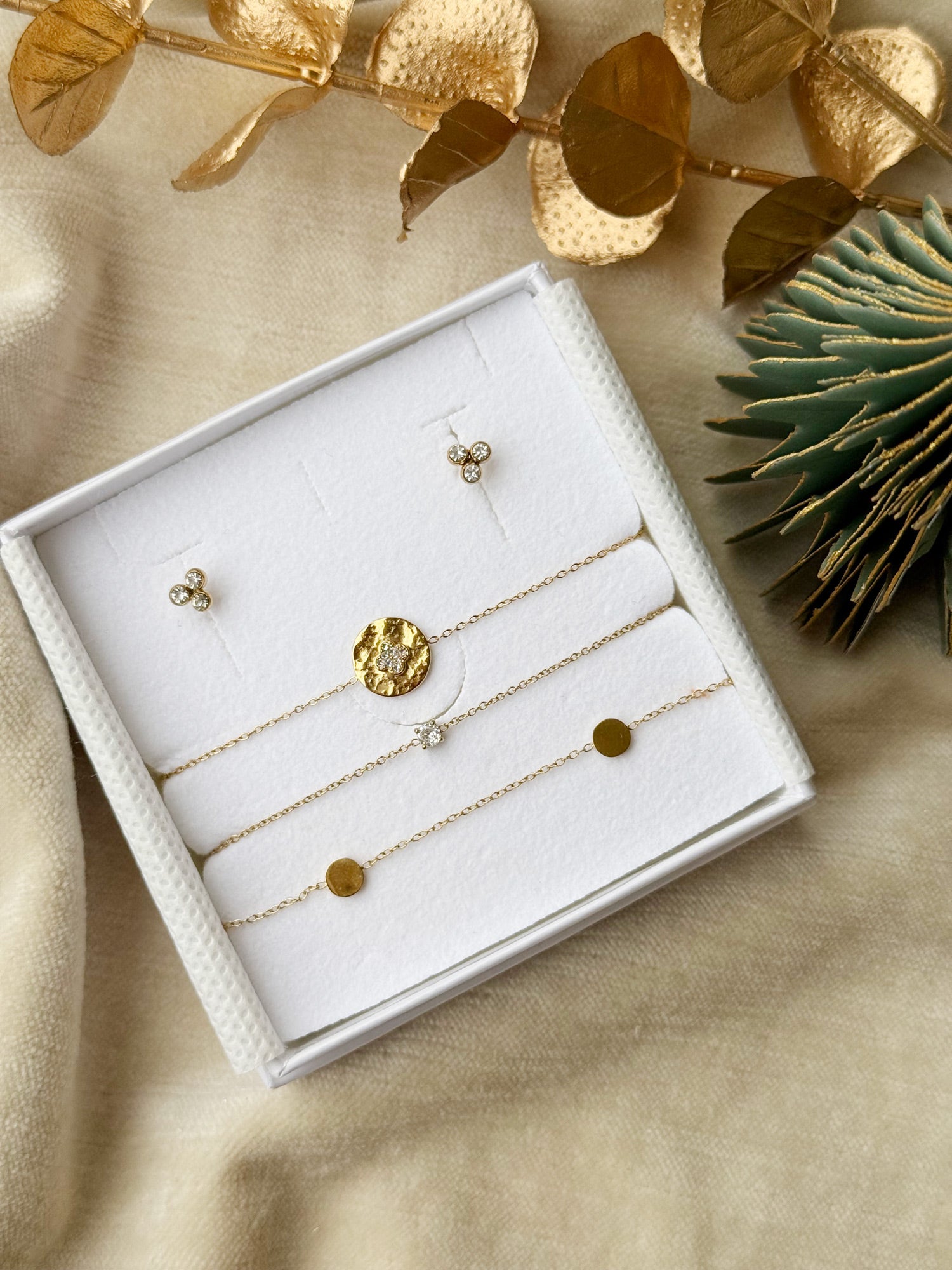 Coffret de parure de bijoux Nova contenant une paire de puces et un trio de bracelets dorés, ornés de zircons - Bijoux photographiés dans un écrin à bijoux blanc dans une ambiance de Noël