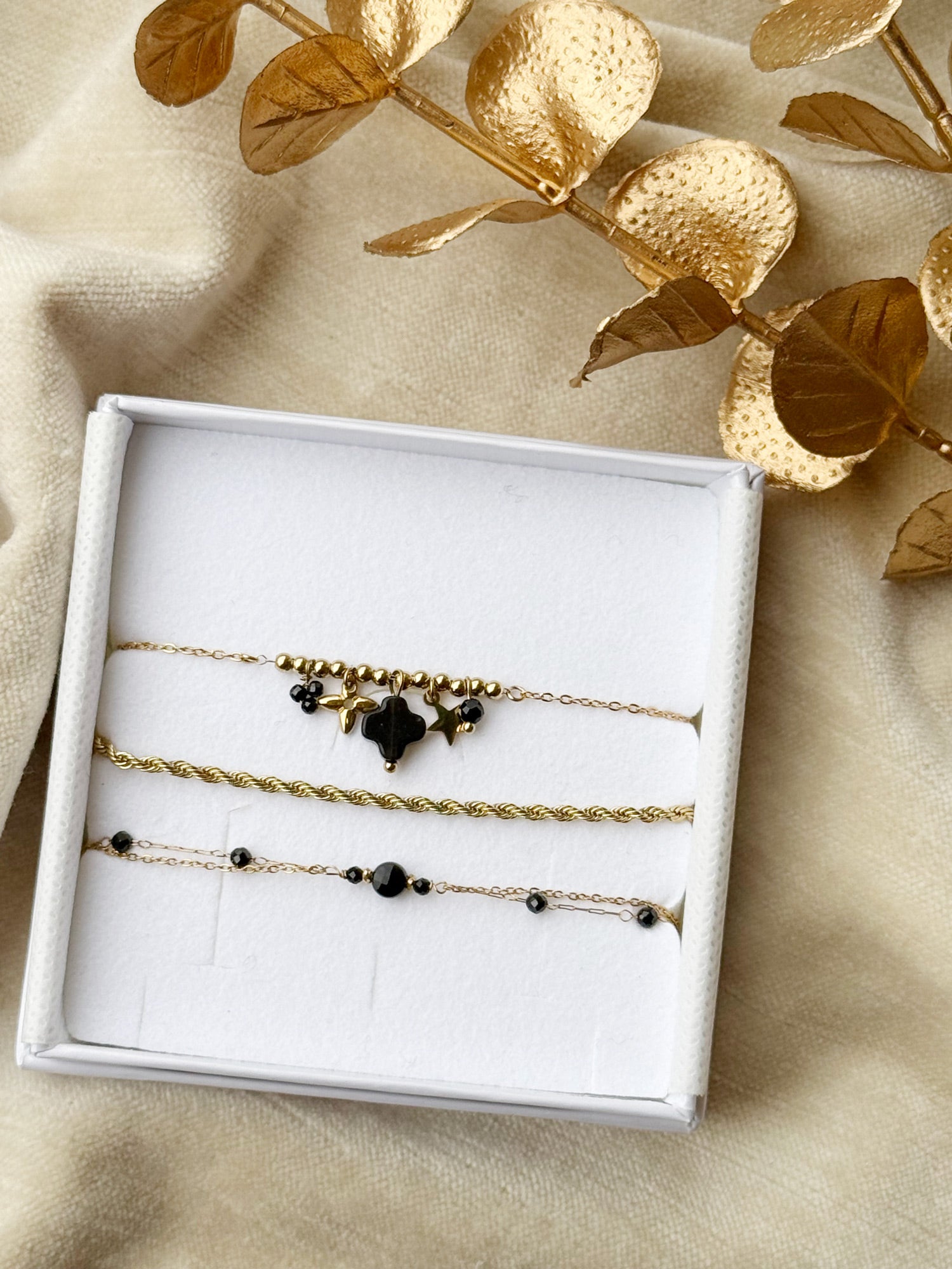 Coffret de parure de bijoux Onyx contenant trois bracelets dorés ornés de pierres naturelles - Bijoux photographié dans un écrin à bijoux blanc dans une ambiance de Noël 
