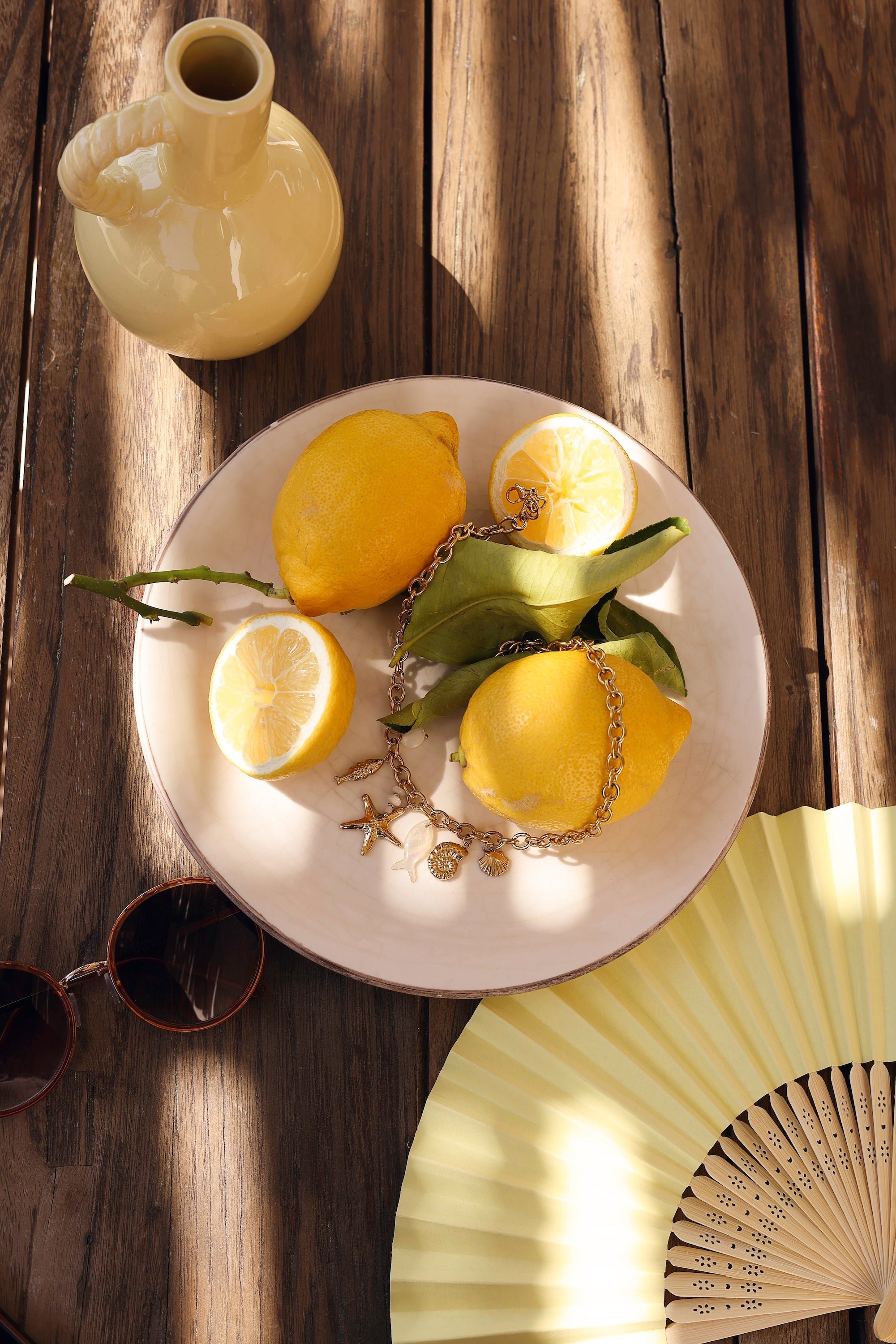 Collier doré Ainoa avec pendentifs poisson, étoile de mer et coquillages - bijou photographié sur assiette blanche avec citrons