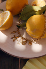 Collier doré Ainoa avec pendentifs poisson, étoile de mer et coquillages - bijou photographié sur assiette blanche avec citrons