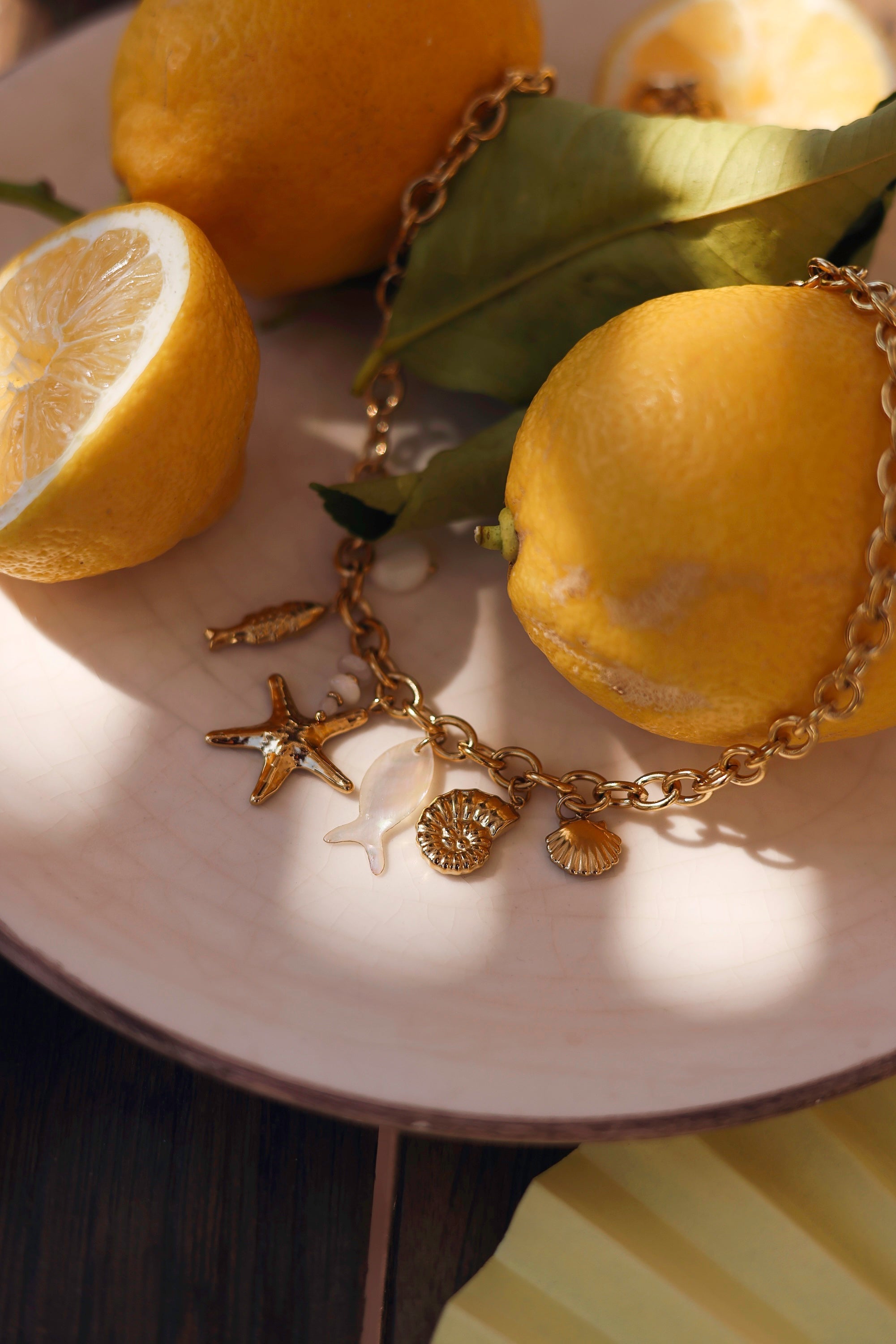 Collier doré Ainoa avec pendentifs poisson, étoile de mer et coquillages - bijou photographié sur assiette blanche avec citrons