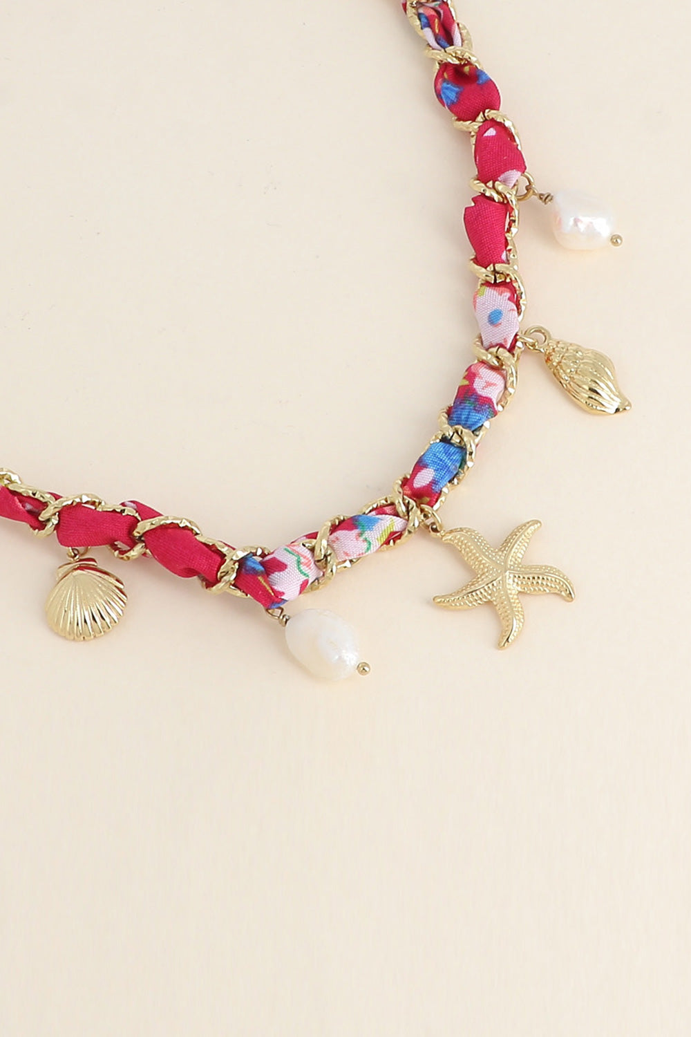 Collier doré Aminata maille entrelacée avec tissu rose fuchsia pendentifs coquillages, étoile de mer et nacres - Bijou photographié sur fond beige