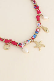 Collier doré Aminata maille entrelacée avec tissu rose fuchsia pendentifs coquillages, étoile de mer et nacres - Bijou photographié sur fond beige