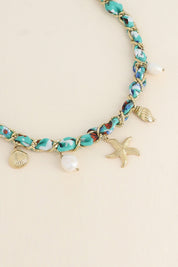Collier doré Aminata maille entrelacée avec tissu turquoise pendentifs coquillages, étoile de mer et nacres - Bijou photographié sur fond beige