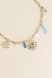 Collier maille doré Maja avec pendentifs coquillages, corail, soleil et pierres naturelles - Bijou photographié sur fond beige