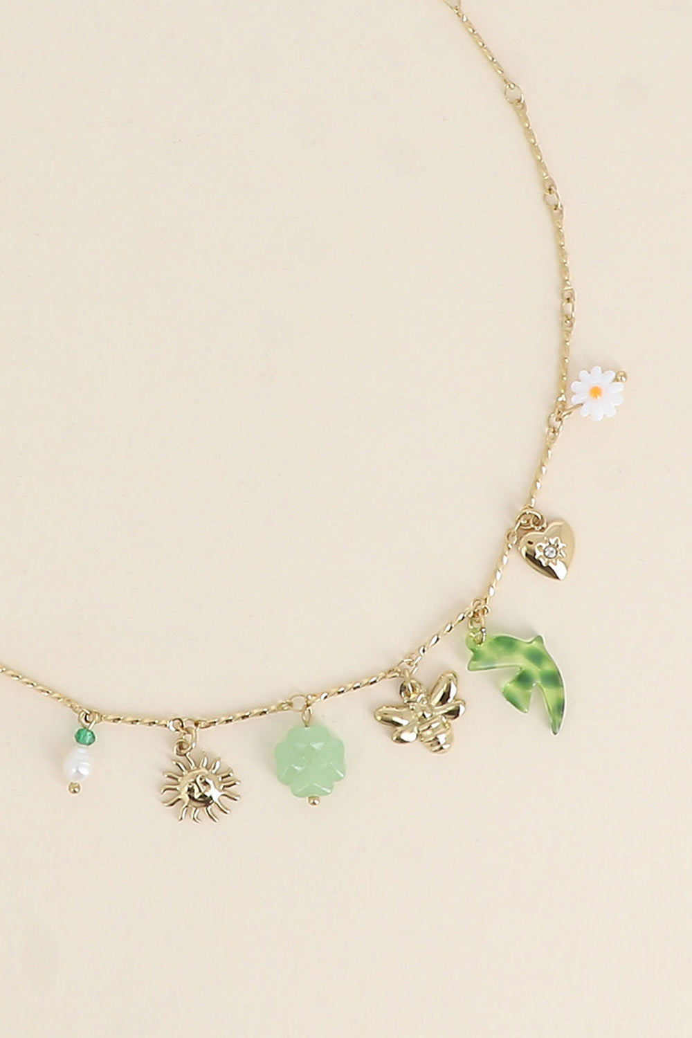 Collier doré Milana chaîne torsadée avec pendentifs soleil, hirondelle, abeille, trèfle, cœur, marguerite et nacre - Bijou photographié sur fond beige