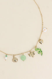 Collier doré Milana chaîne torsadée avec pendentifs soleil, hirondelle, abeille, trèfle, cœur, marguerite et nacre - Bijou photographié sur fond beige