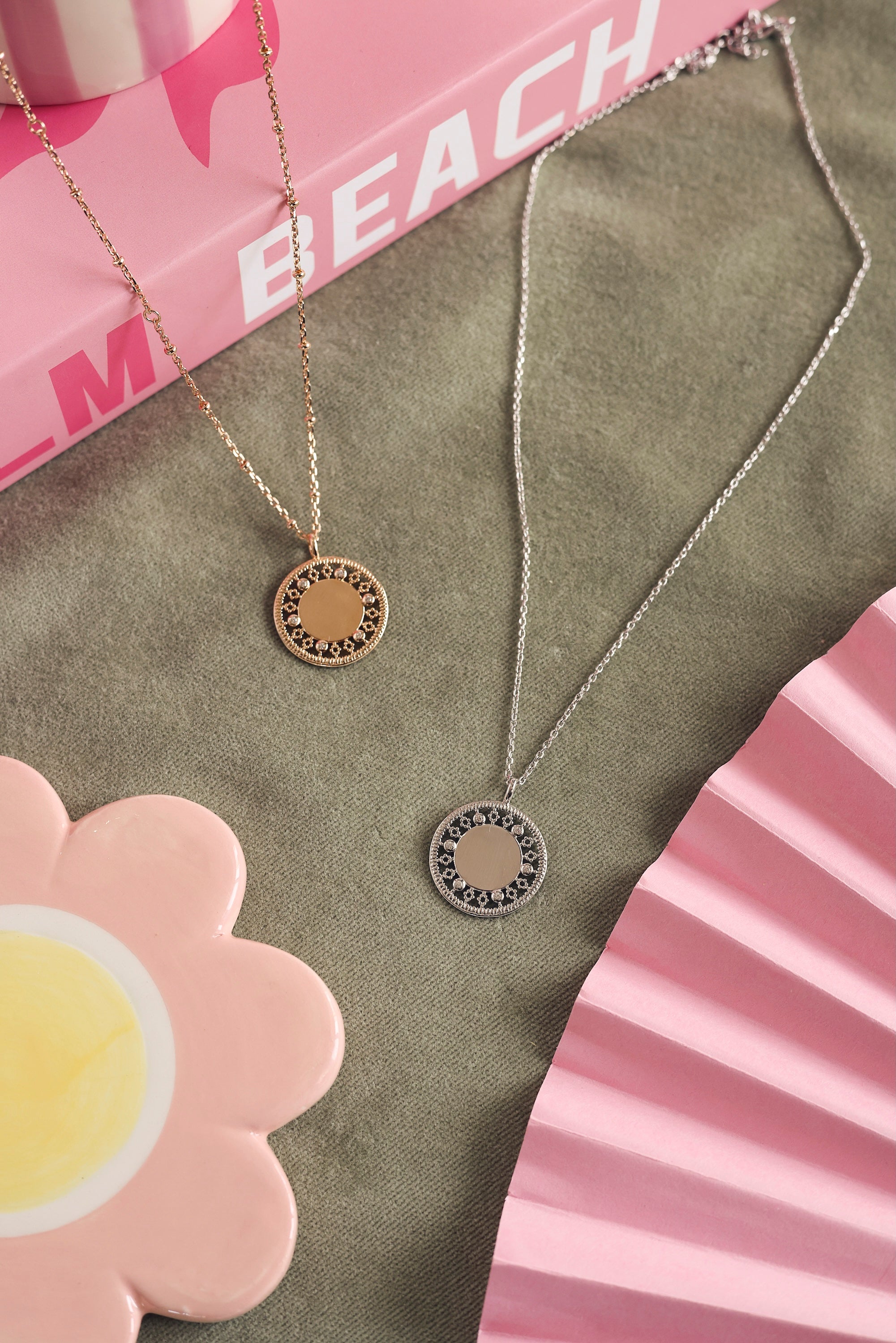 Collier personnalisable Rita en argent avec médaille au contour orné de motifs délicatement ajourés et sertis de zircons - Bijou photographié sur un tissu kaki avec des décorations roses