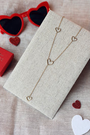 Collier cravate doré Teddi cœurs martelés - Bijou photographié sur un présentoir en lin gris dans une ambiance saint valentin