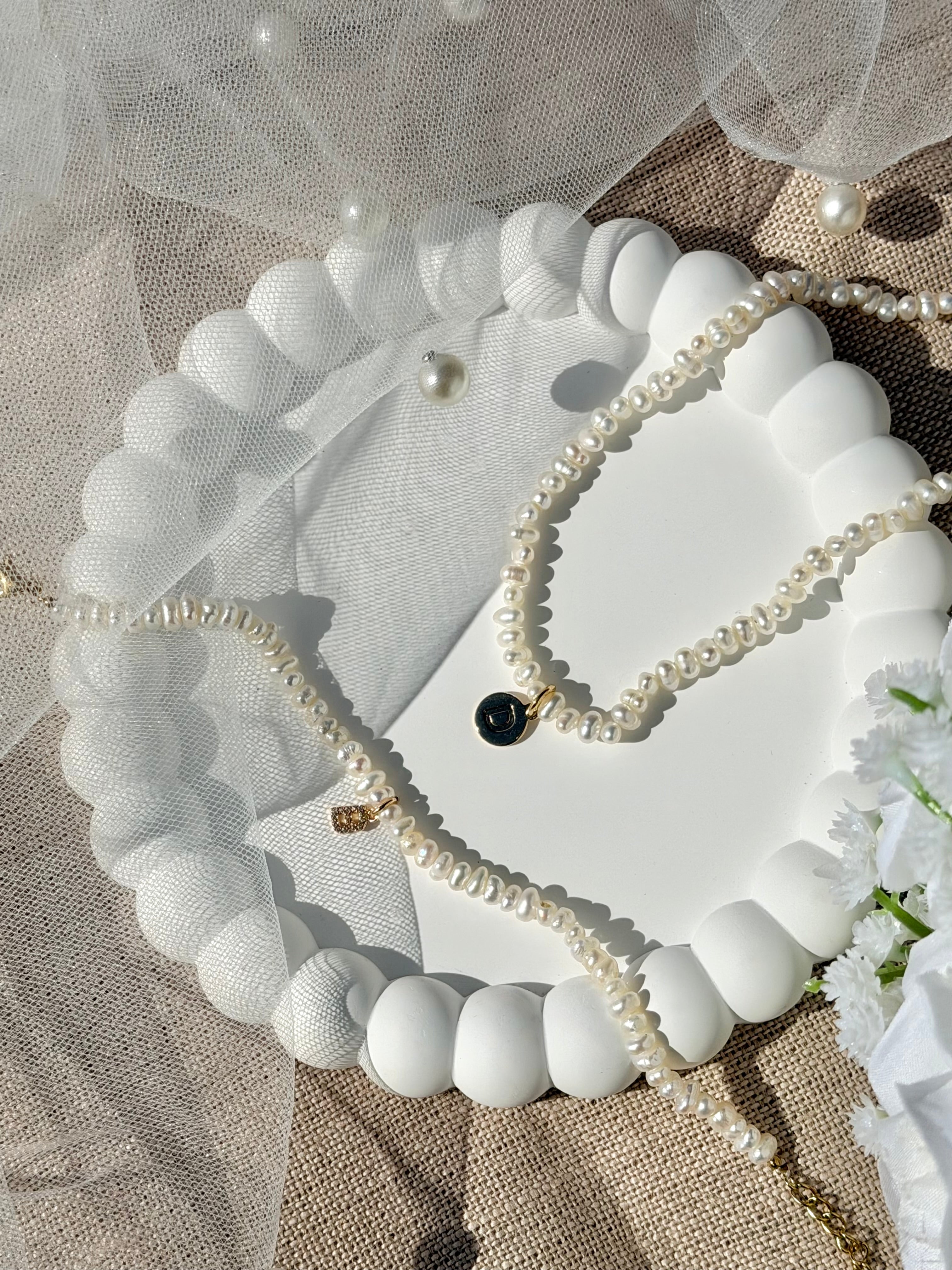 Collier personnalisable Elya doré en nacre pour initiales et charms - Bijou photographié dans une coupole blanche avec un voile de mariée 