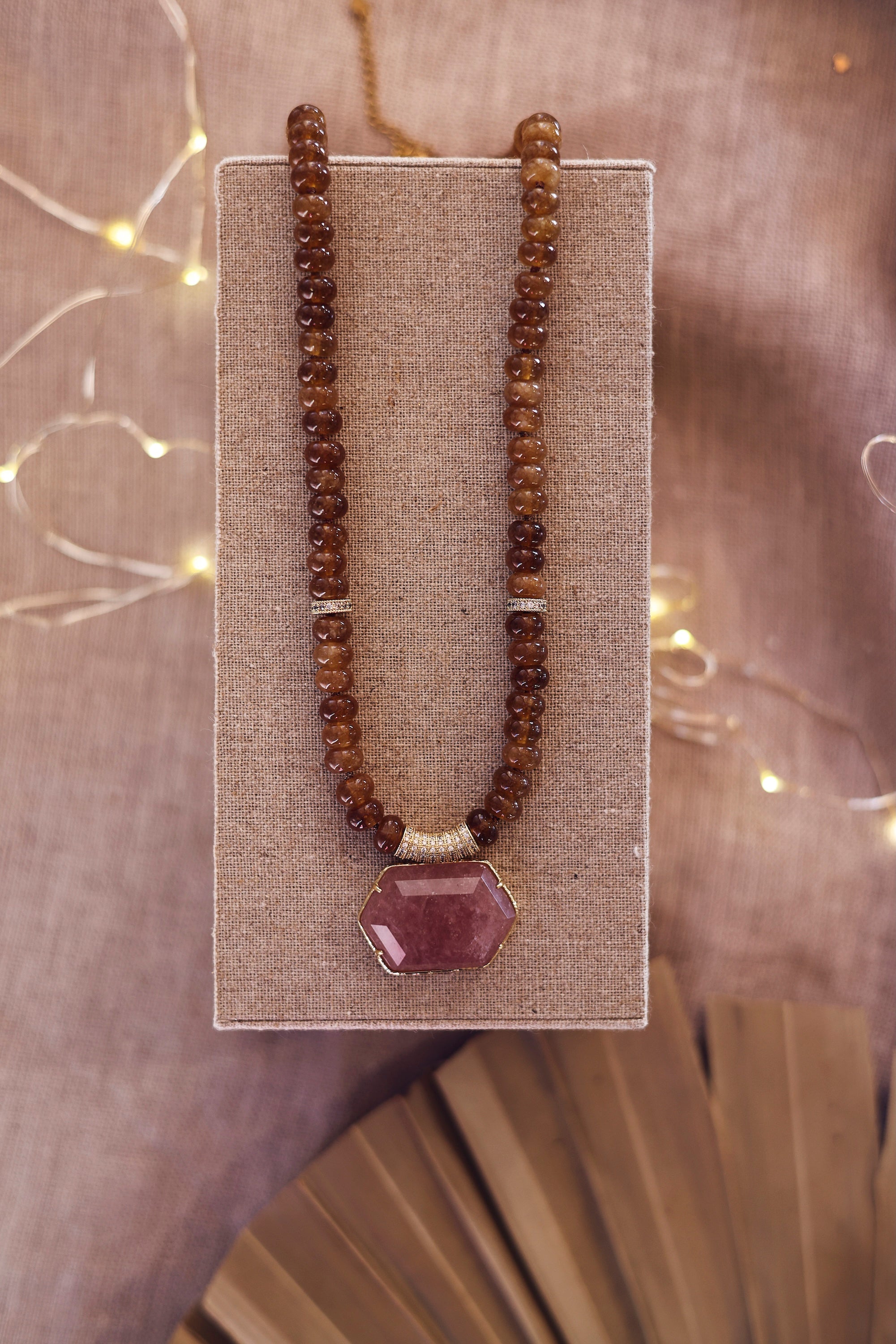 Collier statement doré Isis quartz fumé en pierres naturelles et zircons - Bijou photographié sur un présentoir en lin gris
