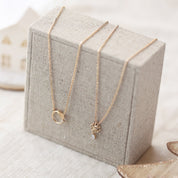 Collier doré nœud de l’infini avec pendentif zircon Joanie - Bijou photographié sur présentoir en lin gris