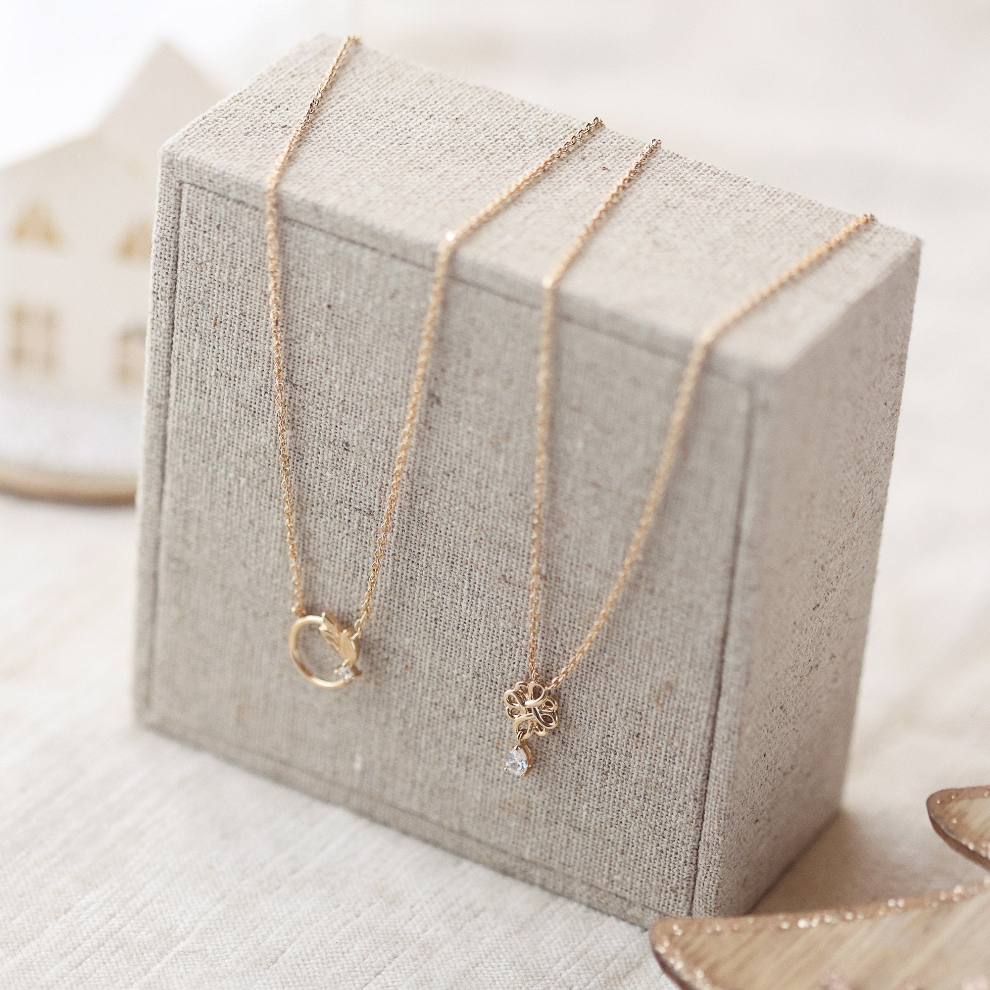 Collier doré nœud de l’infini avec pendentif zircon Joanie - Bijou photographié sur présentoir en lin gris