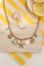Collier doré Livio chaîne en maille avec pendentifs coquillages, étoile de mer, coquillage en nacre, poisson et pierres naturelles - Bijou photographié dans un décor estival